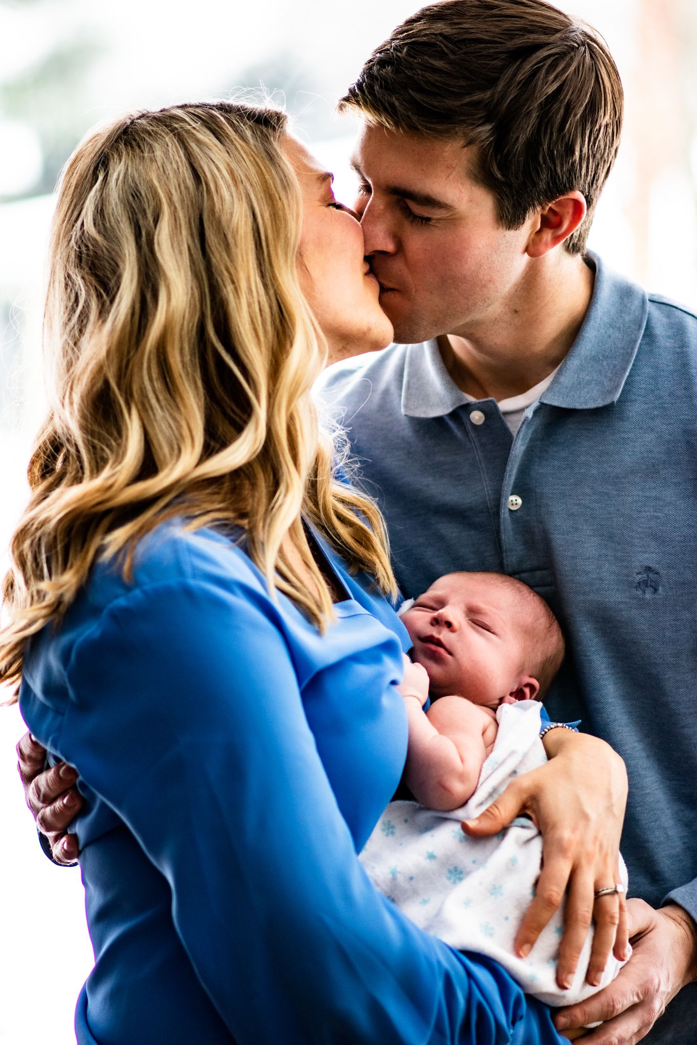 A tender moment between new parents sharing a kiss while holding their newborn baby.
