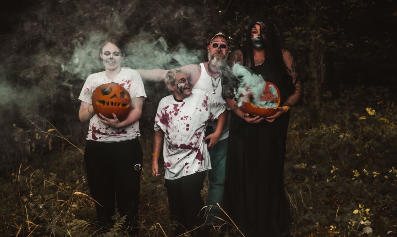 A spooky Halloween family photo with people holding carved pumpkins and wearing zombie makeup.