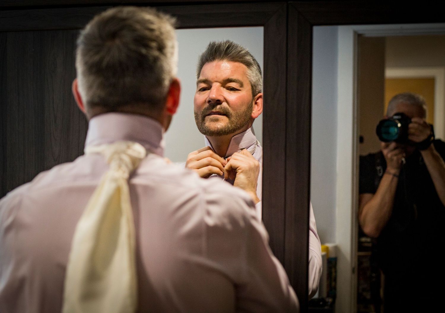 Groomsmen in formal attire gather in a dimly lit room preparing for the wedding ceremony.
