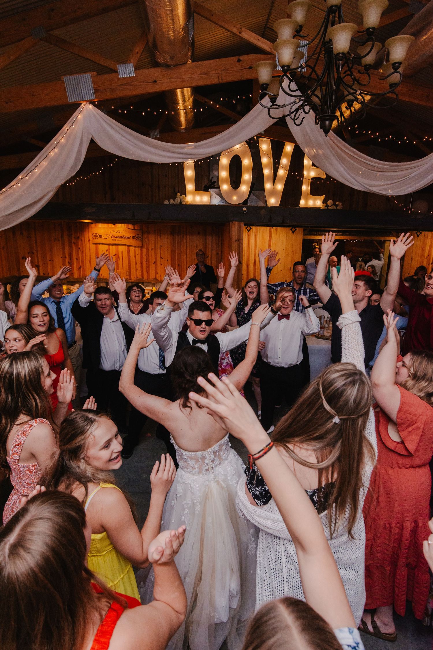 Wedding reception dance party with guests celebrating under LOVE sign and white draping.