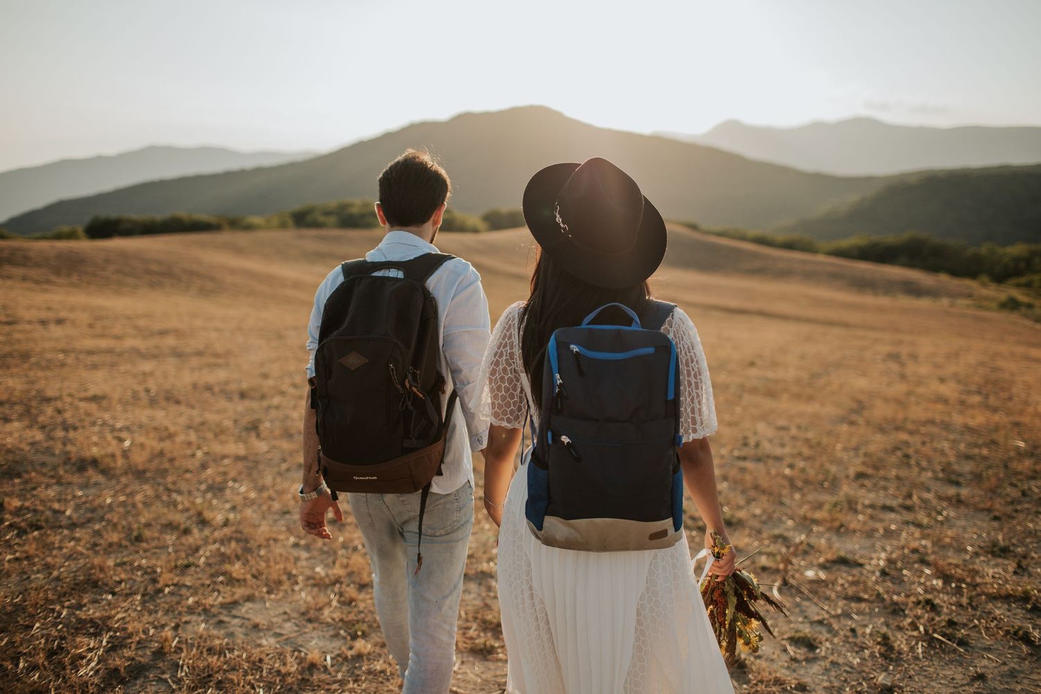 Couple hiking with matching backpacks across a mountainous landscape.
