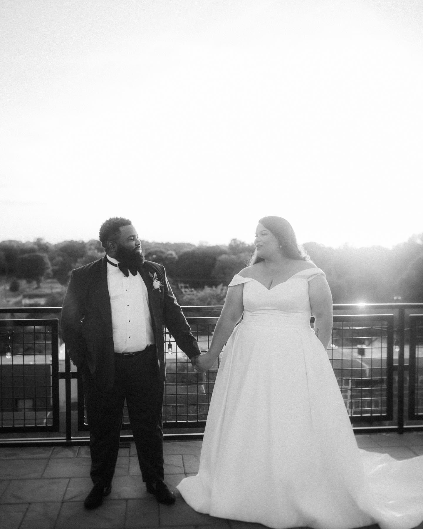 Black and white photo of newlyweds standing together on a balcony at sunset.