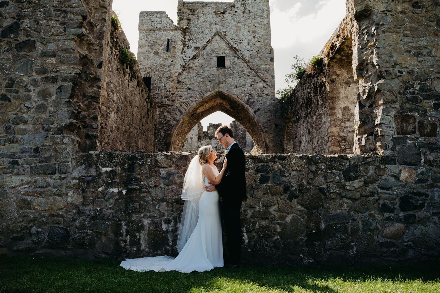 Newly married couple, embrace in front of the castle ruins at Carlingford Priory.