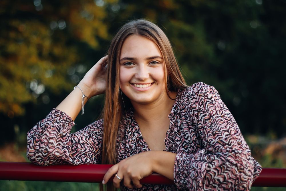 Outdoor portrait session in floral dress with autumn foliage in background.