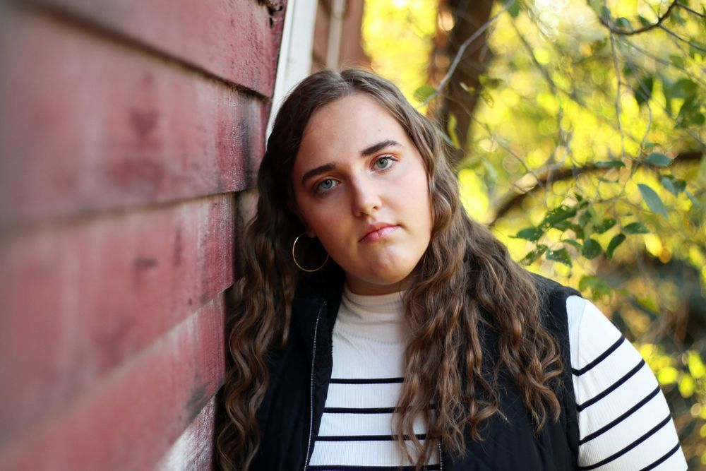 Portrait session in autumn with a striped shirt against a pink wall with golden sunlight filtering through trees.