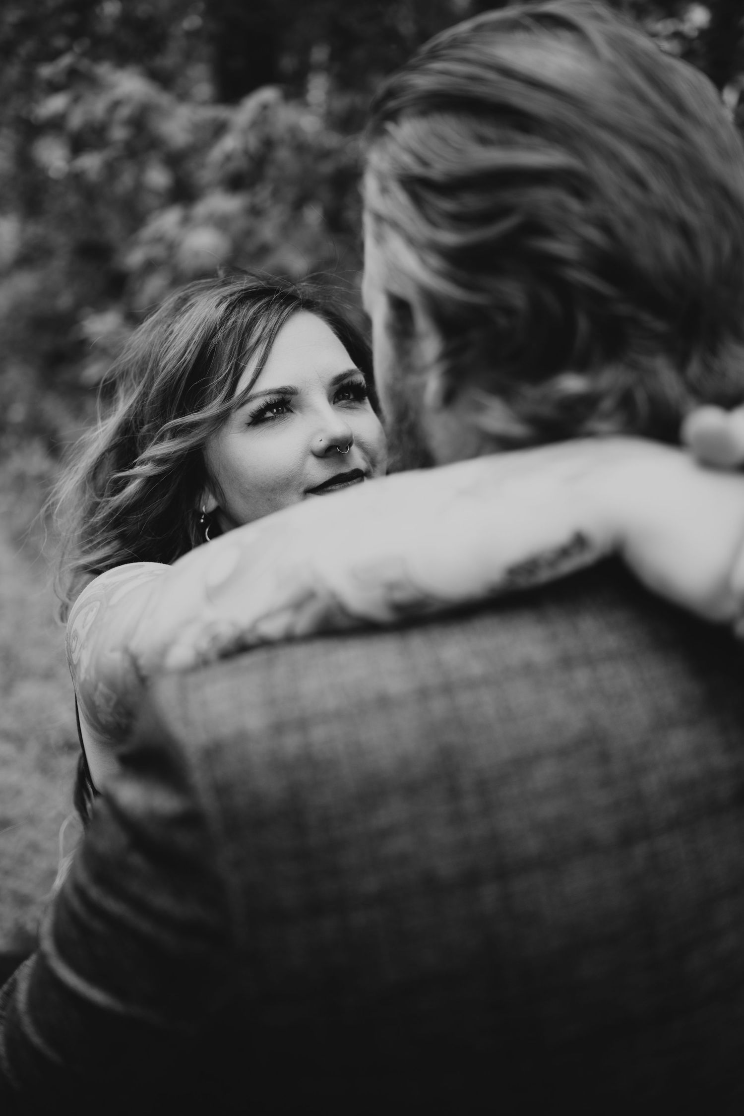 Black and white romantic portrait of a couple embracing outdoors with soft natural lighting and bokeh background.