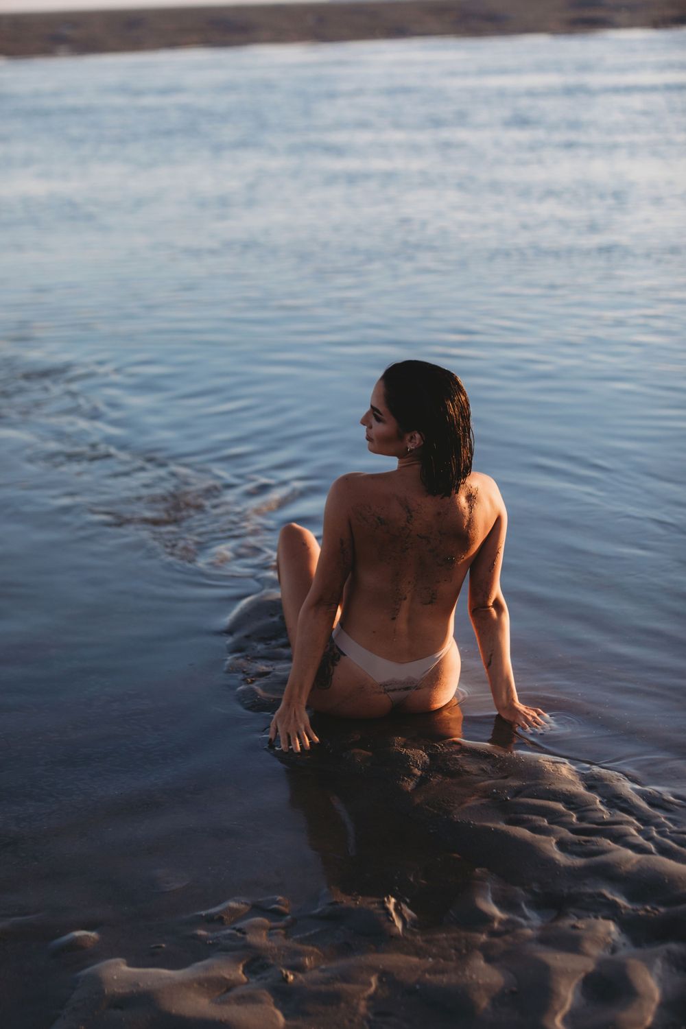 Artistic sunset photo of figure resting on rocky shore in water.