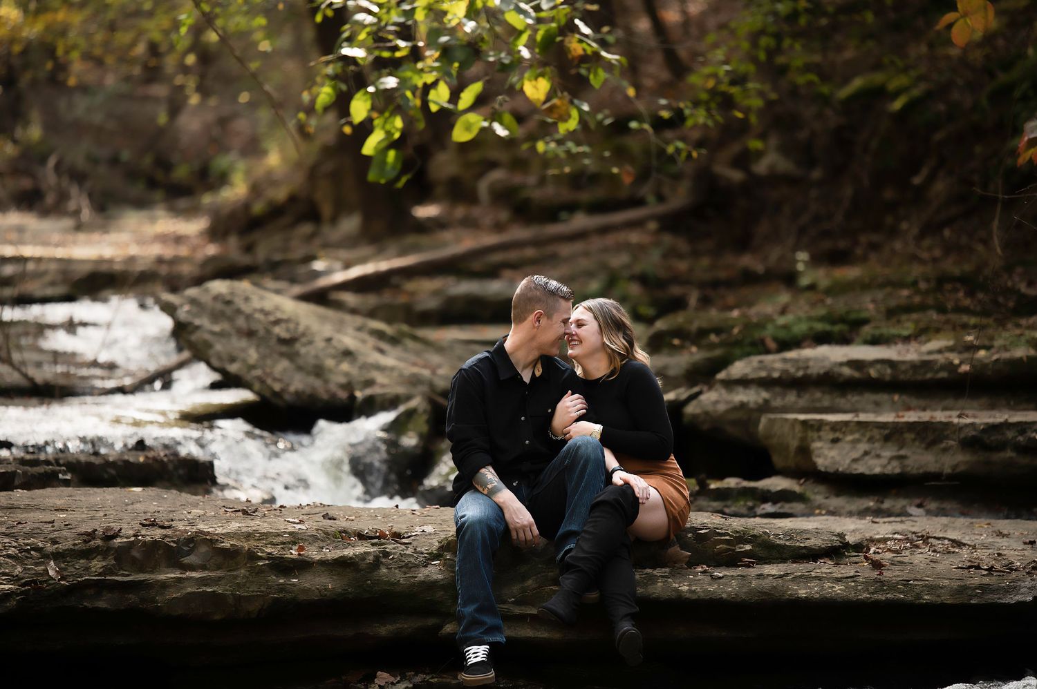 Couple shares romantic moment on rocky riverbank in nature setting.