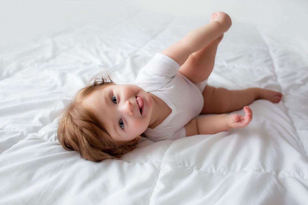 6 month old baby boy playing with feet looking at camera and sticking out tongue.