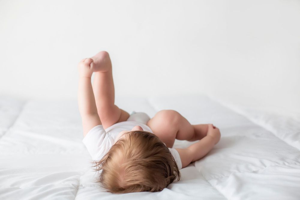 6 month old baby boy laying on white blanket playing with his toes.
