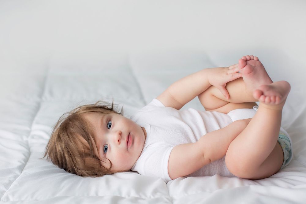 6 month old baby boy laying on his back playing with his feet.