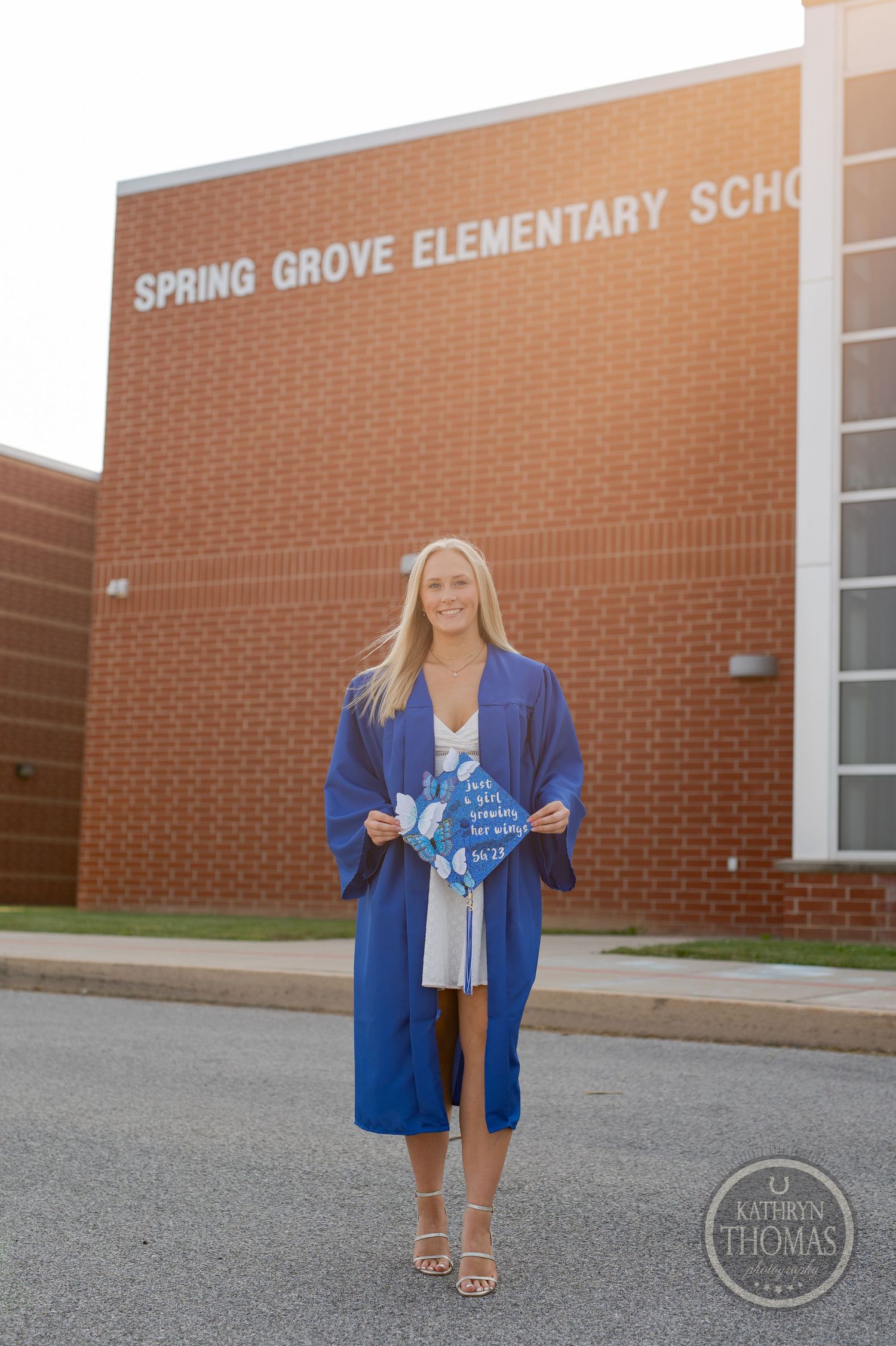 Graduate poses with decorated cap in front of Spring Grove Elementary School.