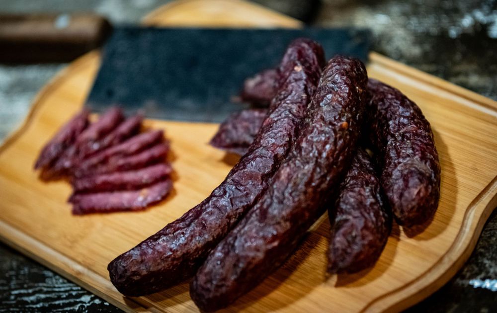 Close-up of dark red cured sausages displayed on a wooden cutting board.