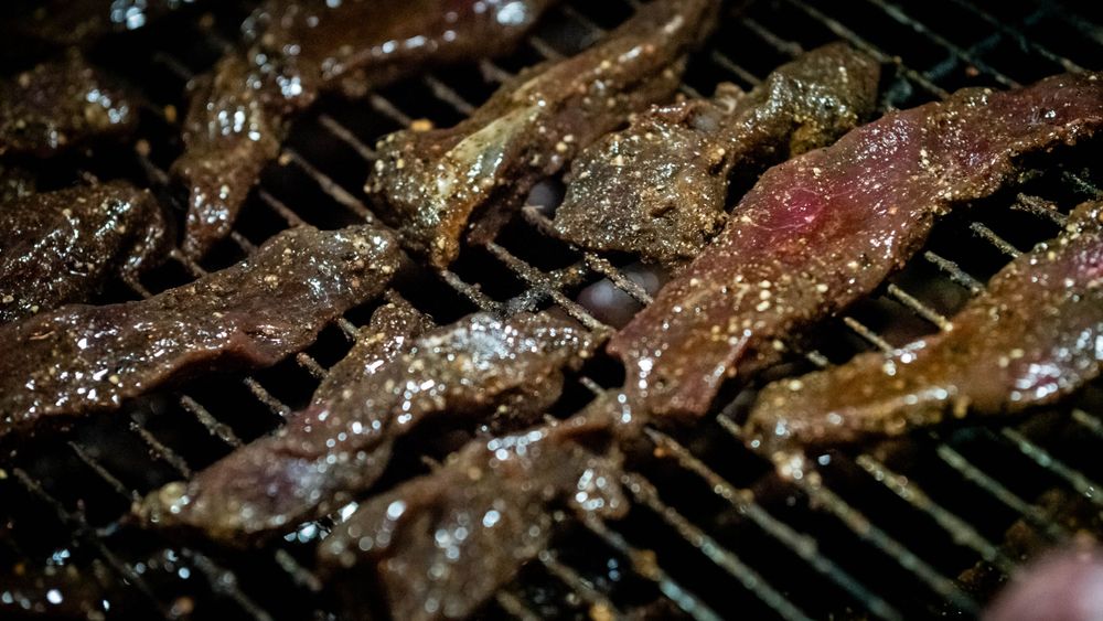 Marinated meat strips sizzling on a hot grill with visible seasonings.