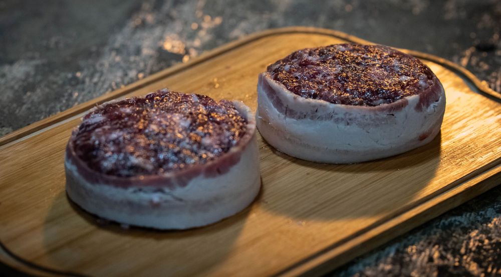 Two grilled burger patties with caramelized crusts on a wooden serving board.