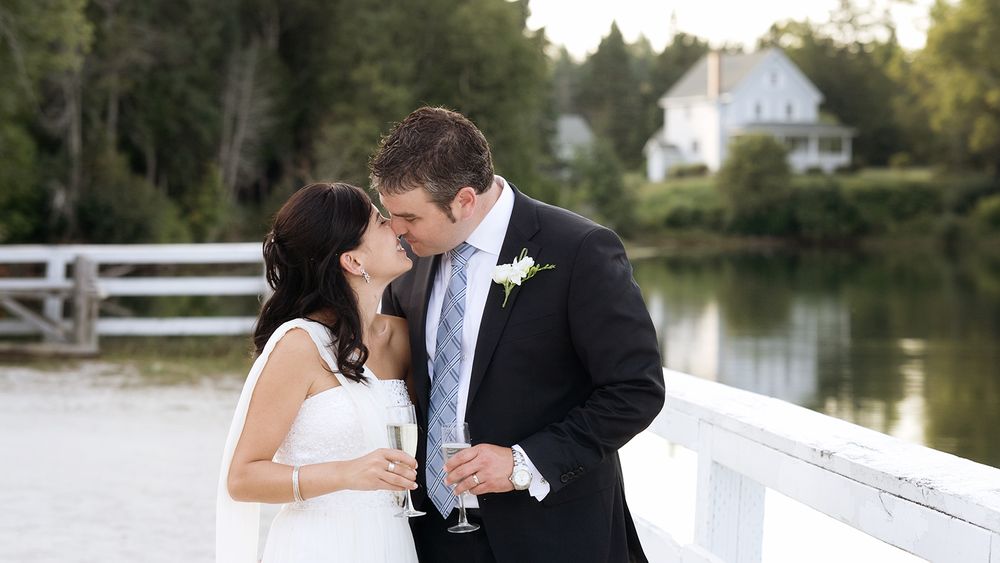 Romantic wedding couple sharing intimate moment on white dock by lake.