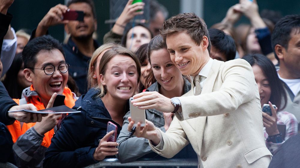 Crowd of excited fans taking selfies with phones at outdoor event.