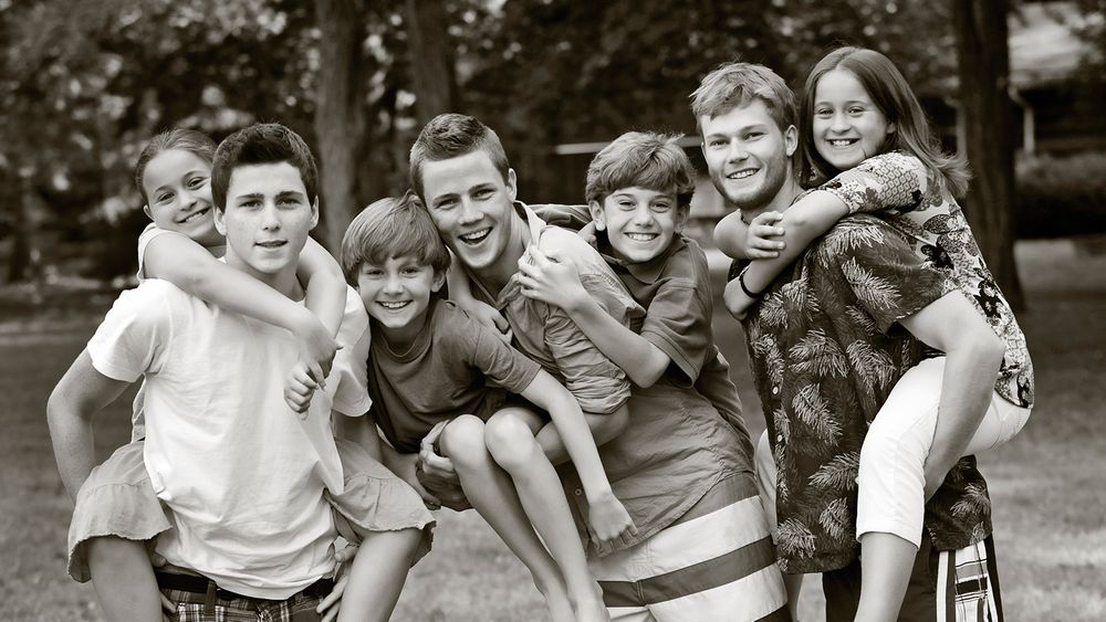 Black and white photograph of playful group carrying each other piggyback style outdoors.