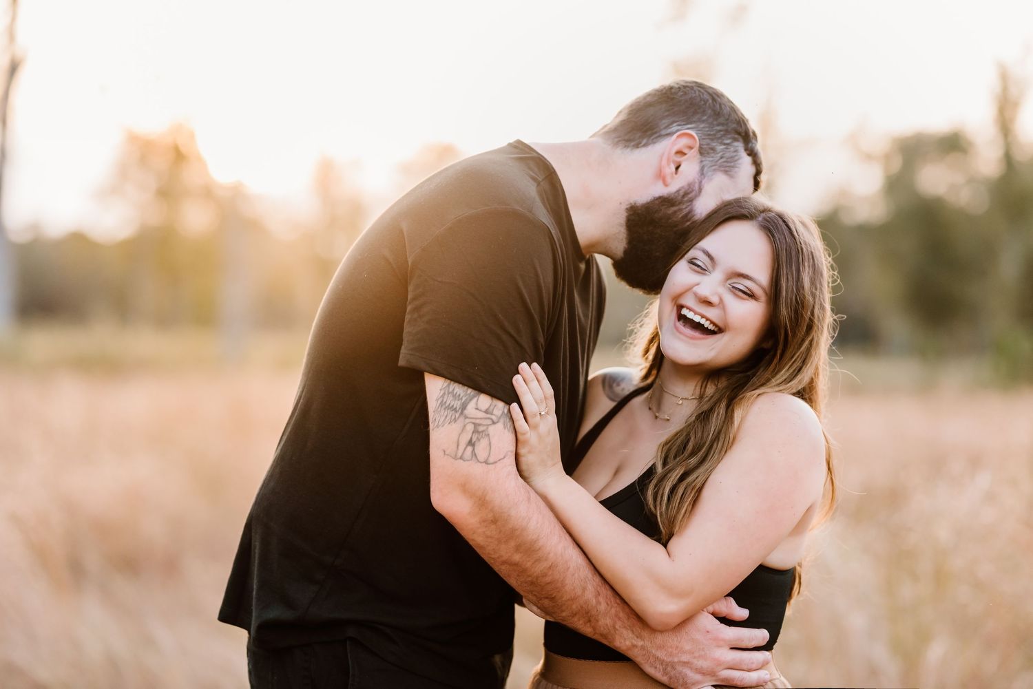 A couple shares a tender moment while laughing together in a sunlit field.