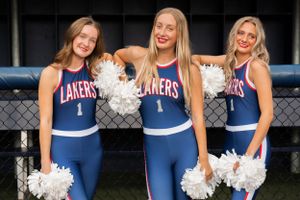 High School Dancers in blue Lakers uniforms pose with white pom poms in front of a chain link fence.