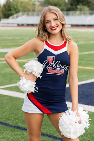 High School Dancer in navy and red Lakers uniform poses with white pom poms on a football field.