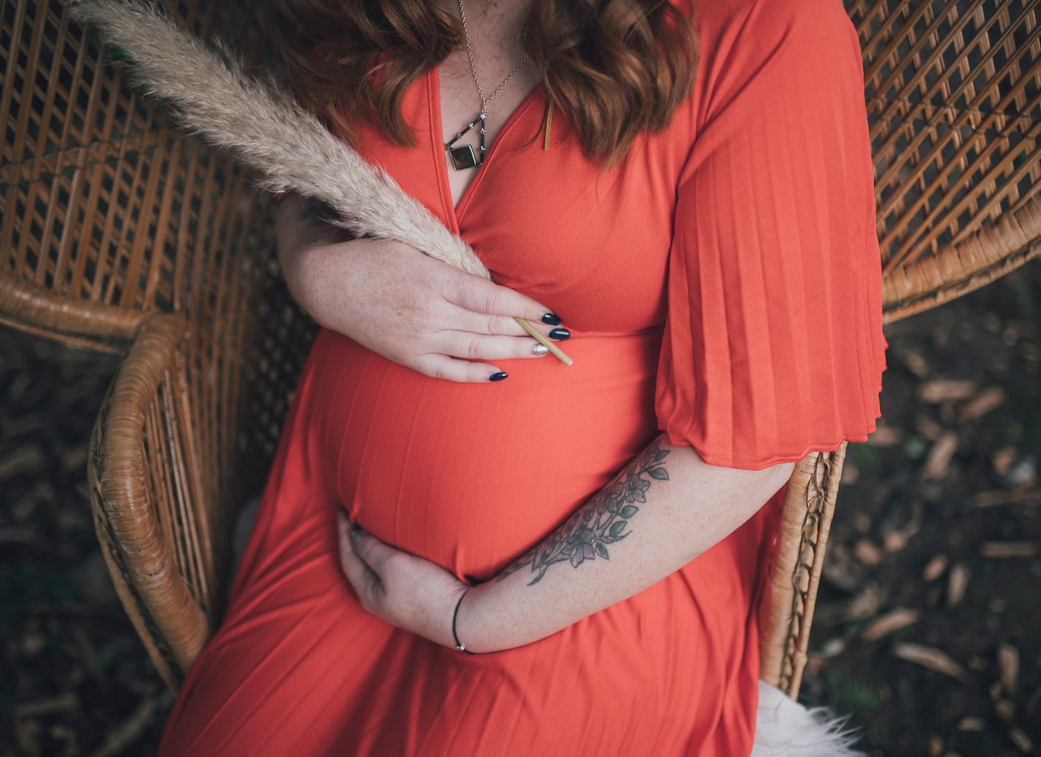 Maternity session featuring woman in coral dress against woven backdrop at sunset. Worcestershire Wedding photographer.