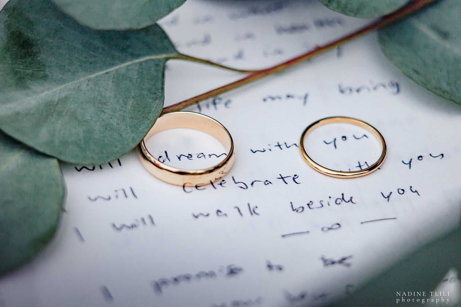 Two golden wedding rings resting on handwritten vows with eucalyptus leaves.