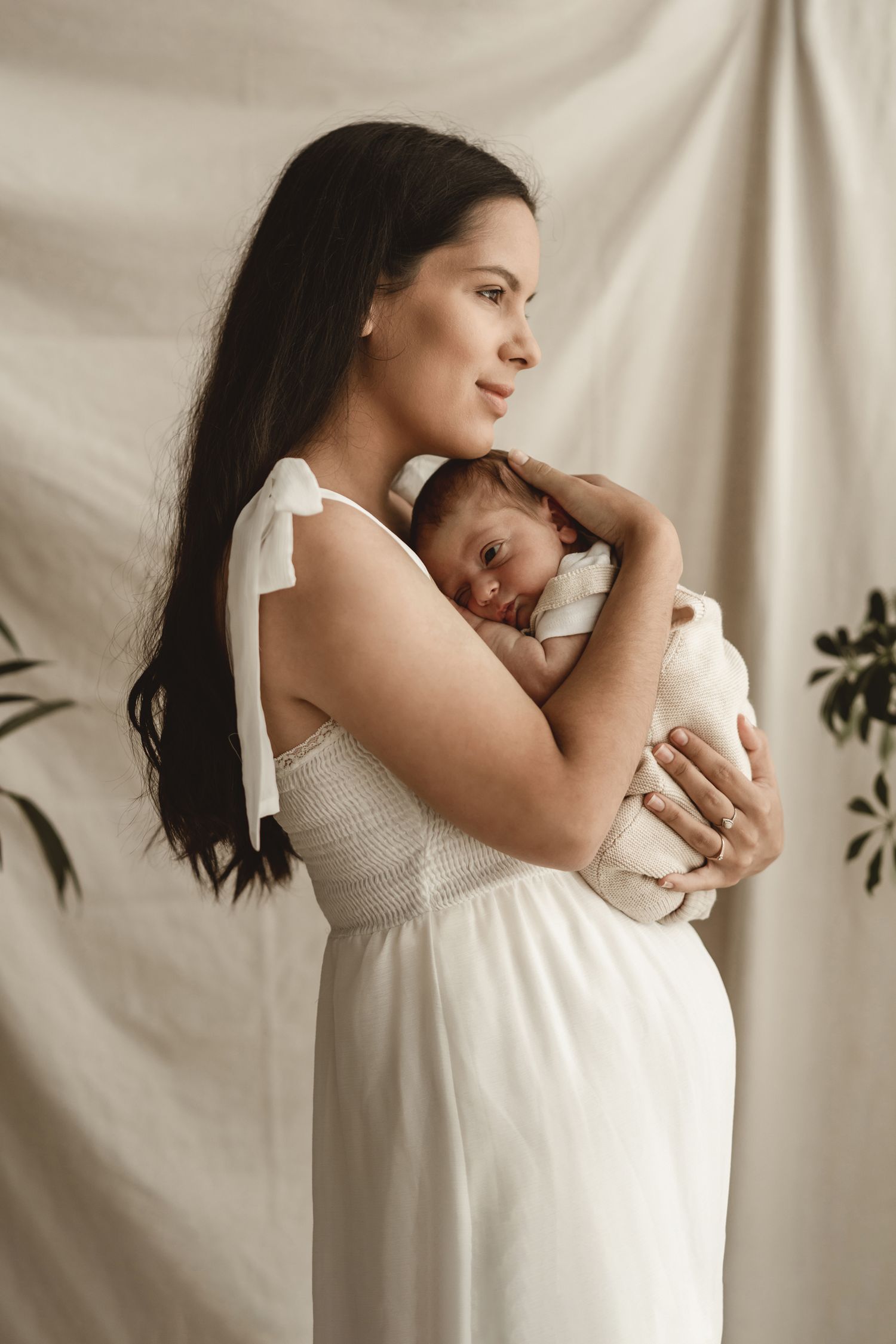 Elegant studio portrait with white fabric backdrop showing intimate maternal moment.