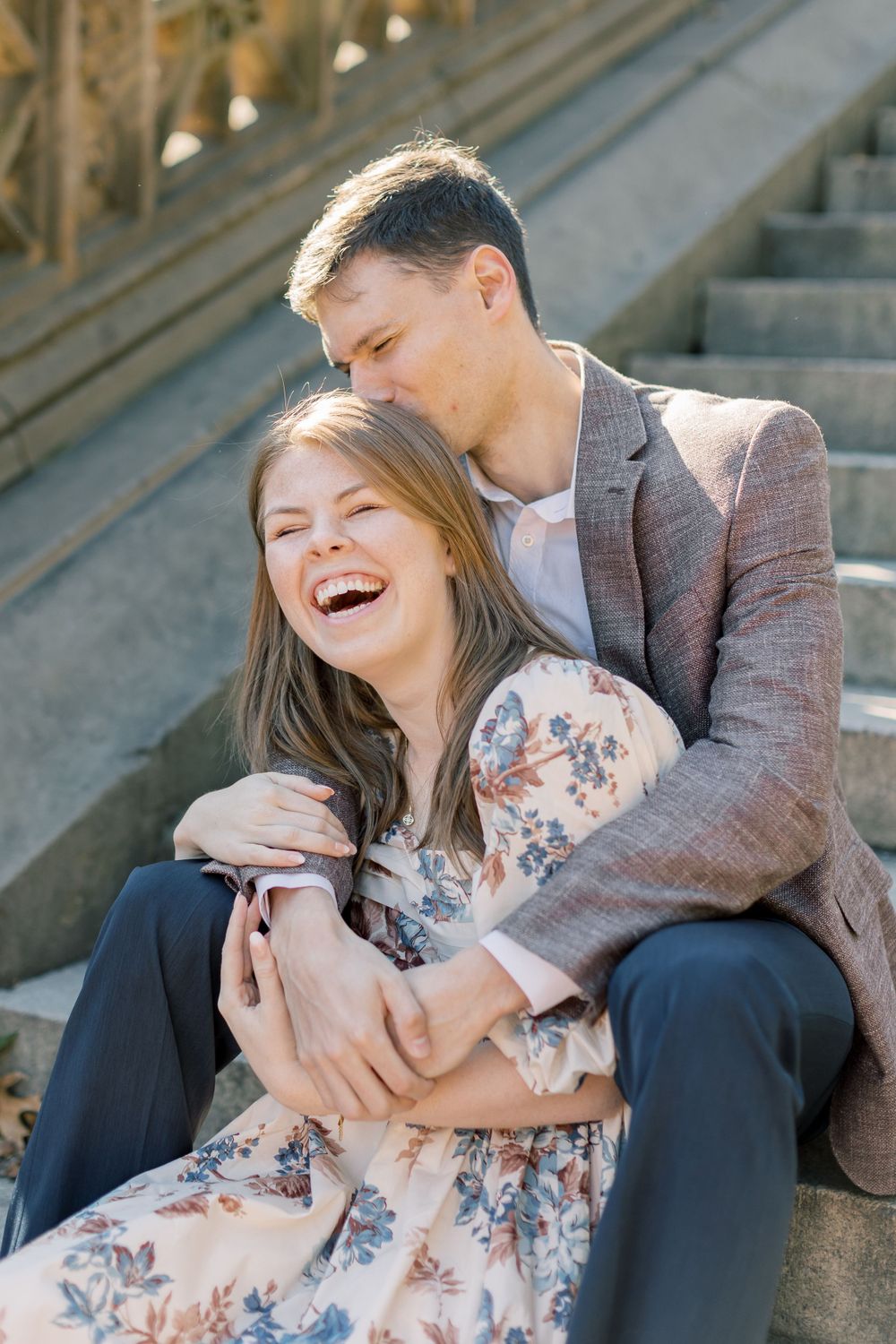 Couple shares laughter while sitting on stone steps during autumn engagement session.
