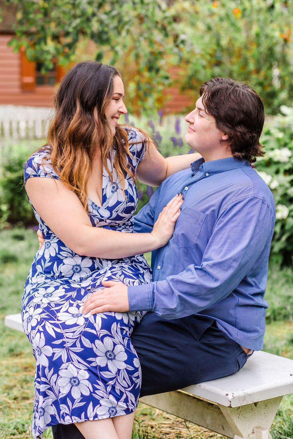 Loving couple shares tender moment in garden setting while wearing blue floral dress and button down shirt.