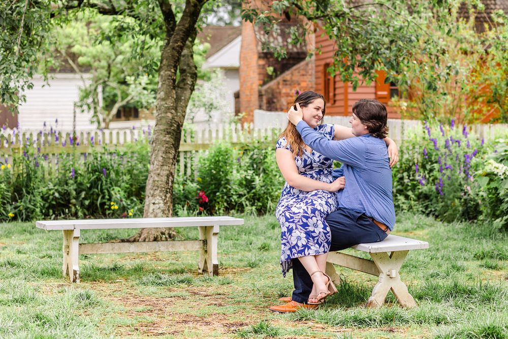 A couple shares a romantic moment on a wooden bench in a garden setting.