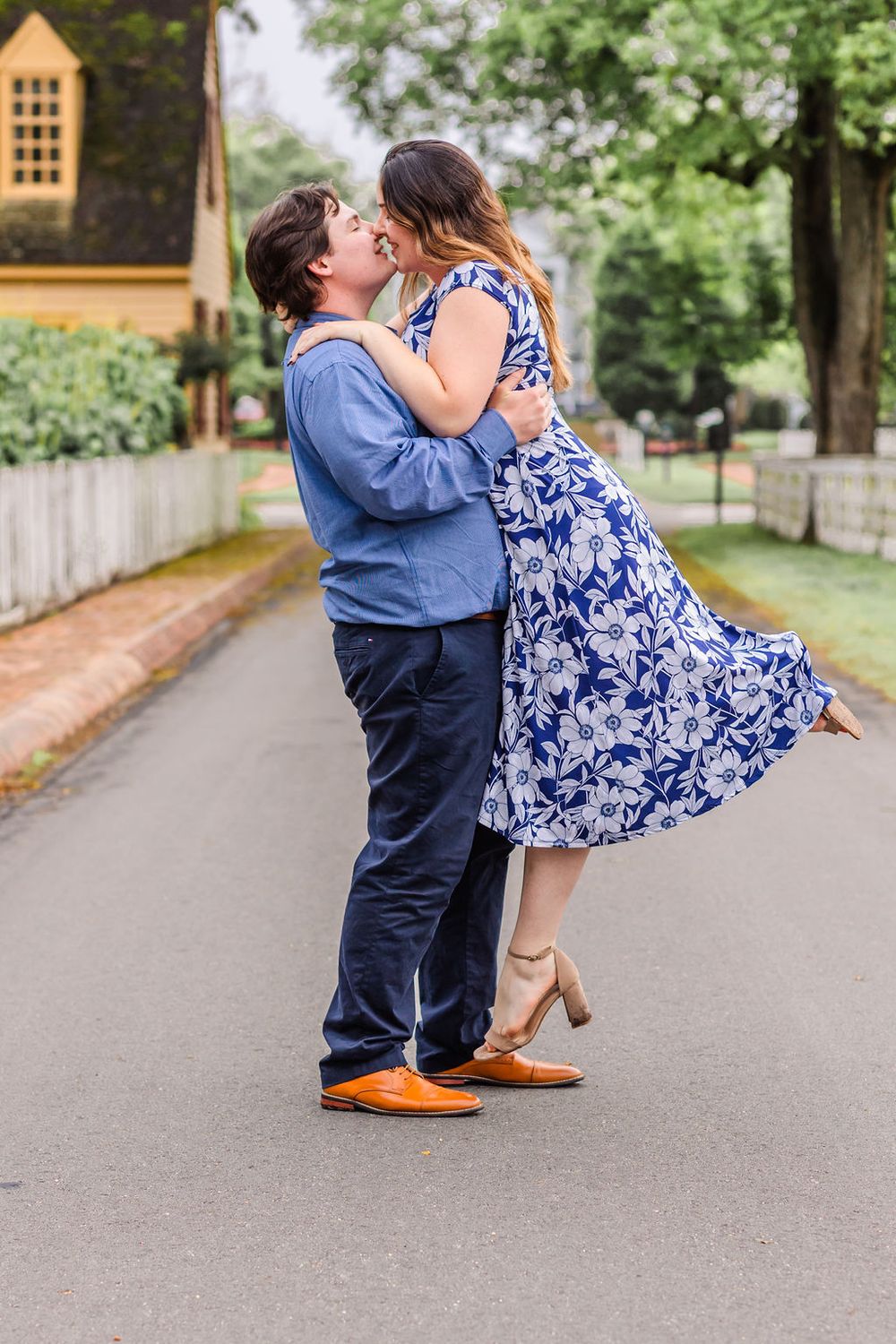 A romantic couple shares a dance moment on a pathway surrounded by trees.