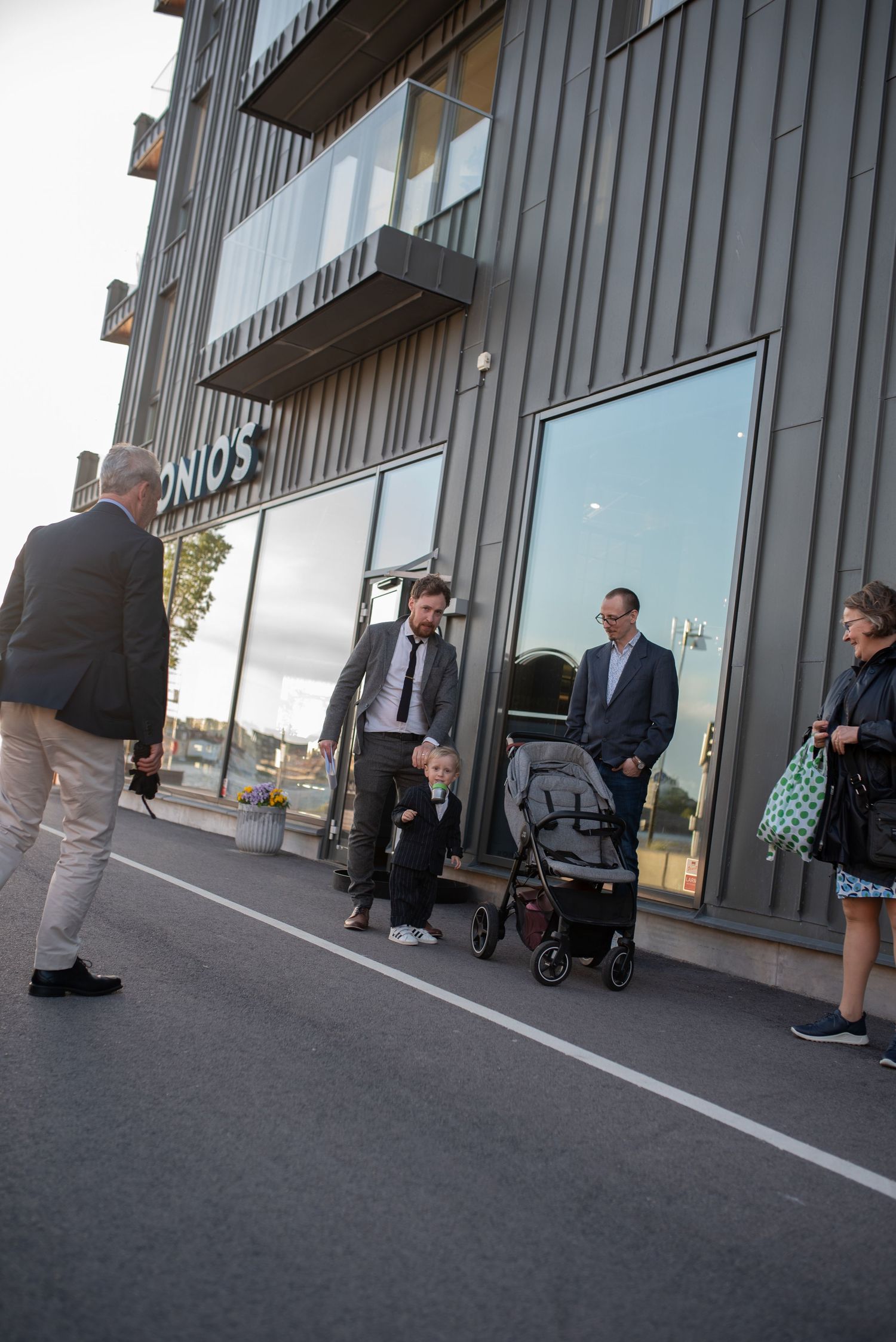 Group gathered outside modern building with stroller and glass facade.