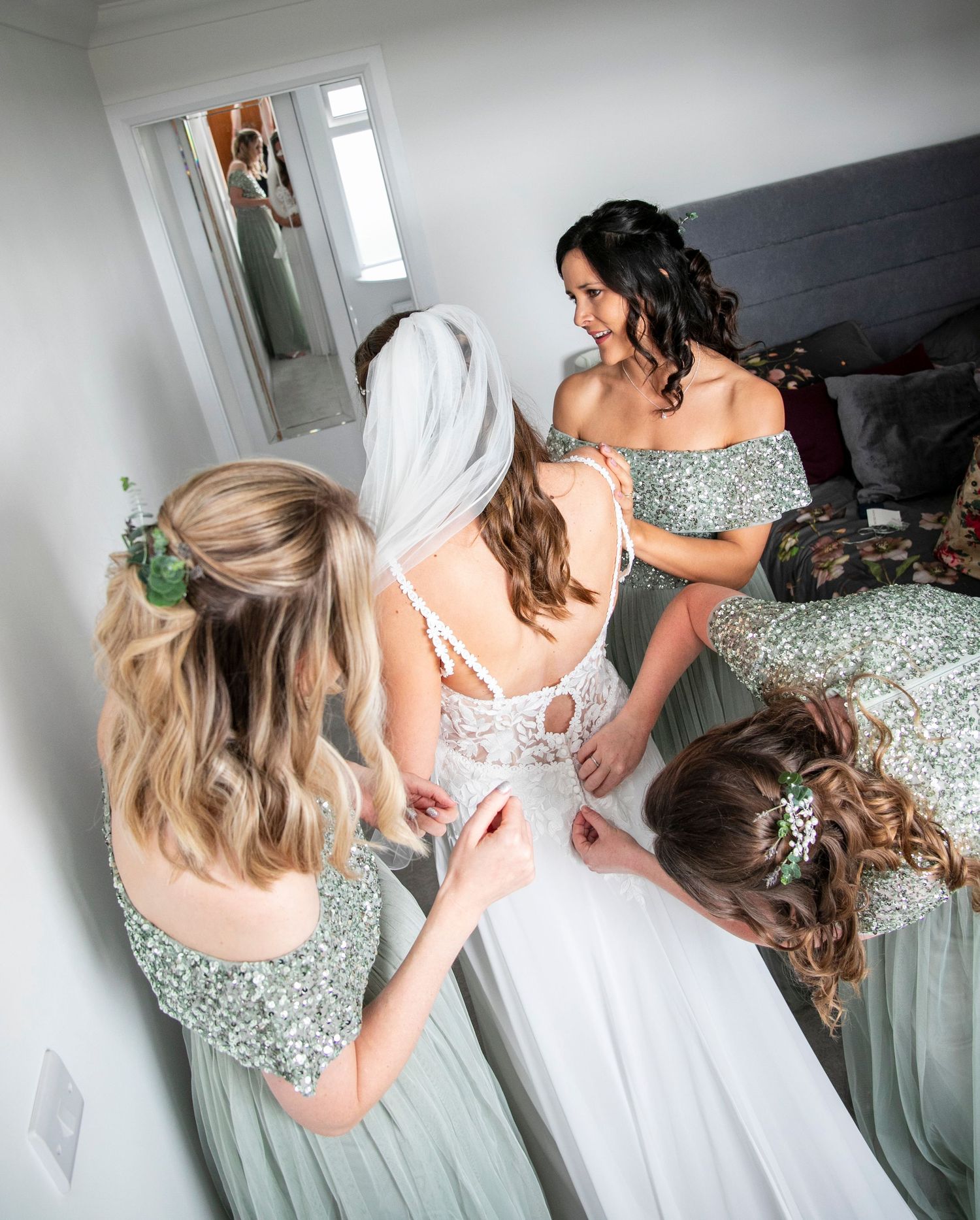 Wedding preparation scene showing mint green bridesmaid dresses and white bridal gown being fastened.