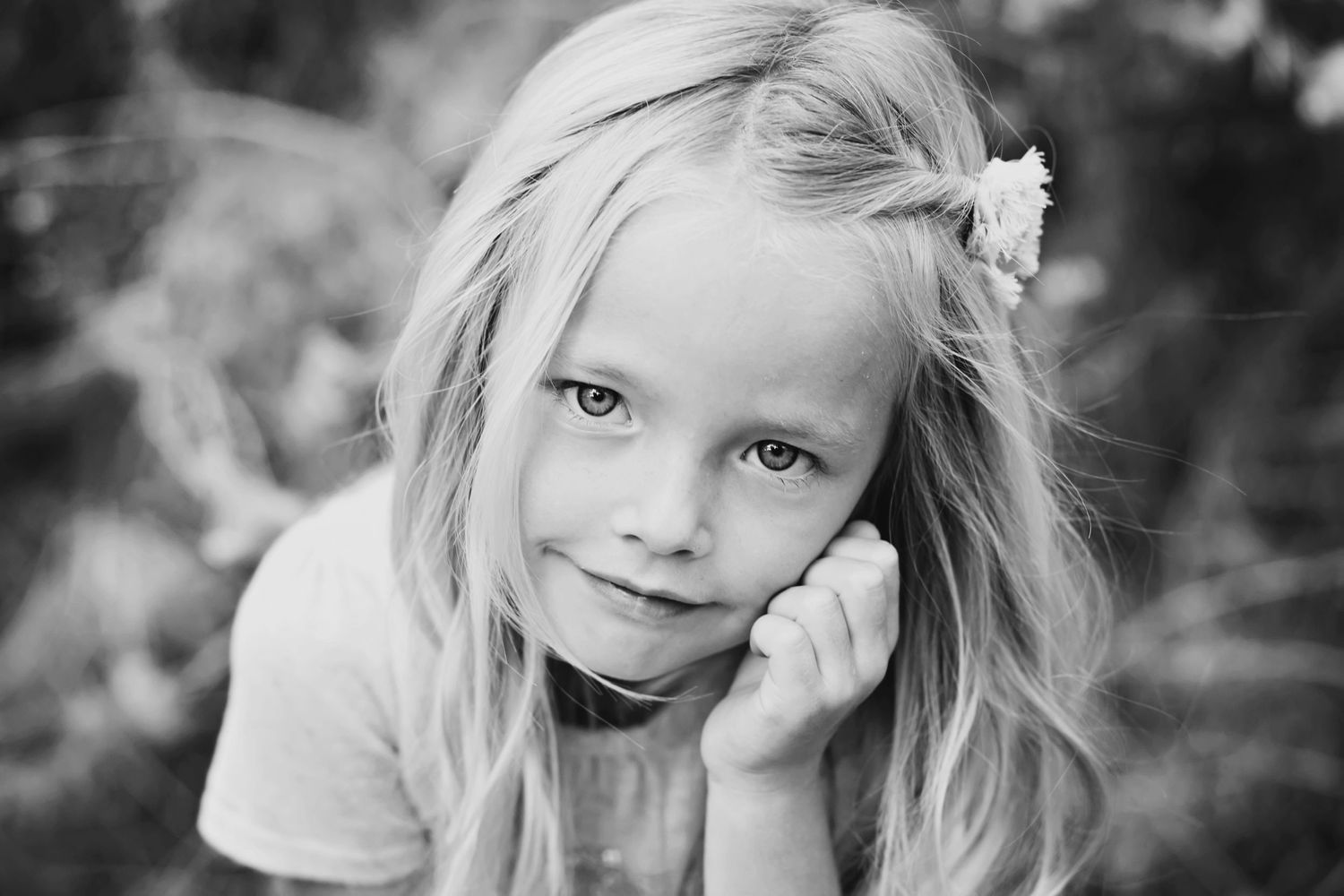 Artistic black and white close-up portrait of a child with blonde hair and flower accessory.