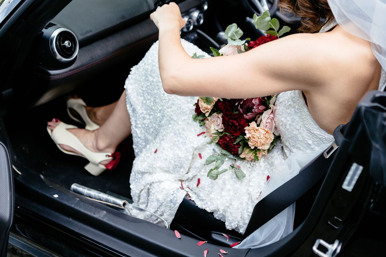 A bride covered in lose petals from her bouquet gets out of a car before the reception of her wedding in Italy.
