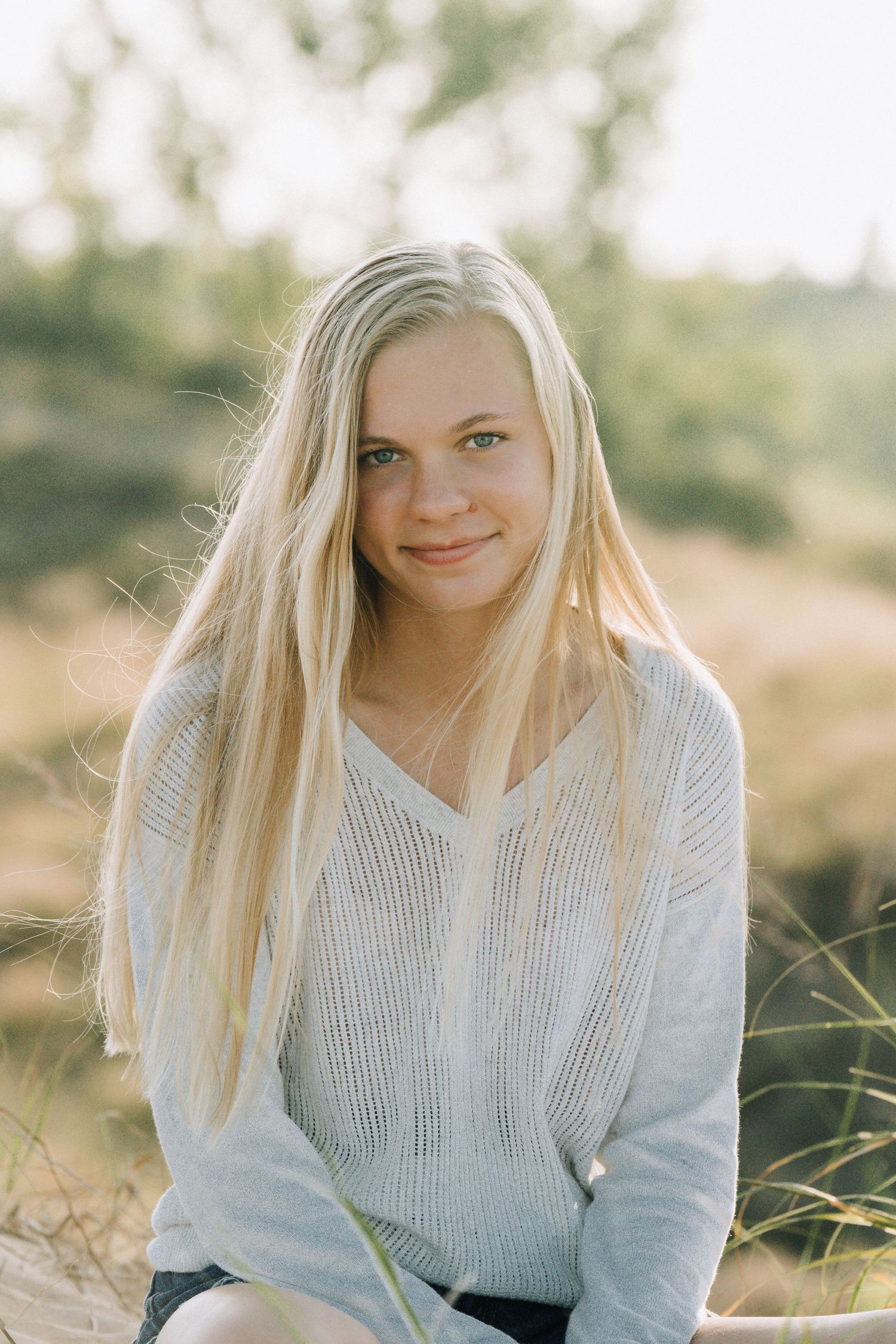 Portrait of someone in a cozy white knit sweater sitting outdoors in warm natural lighting.