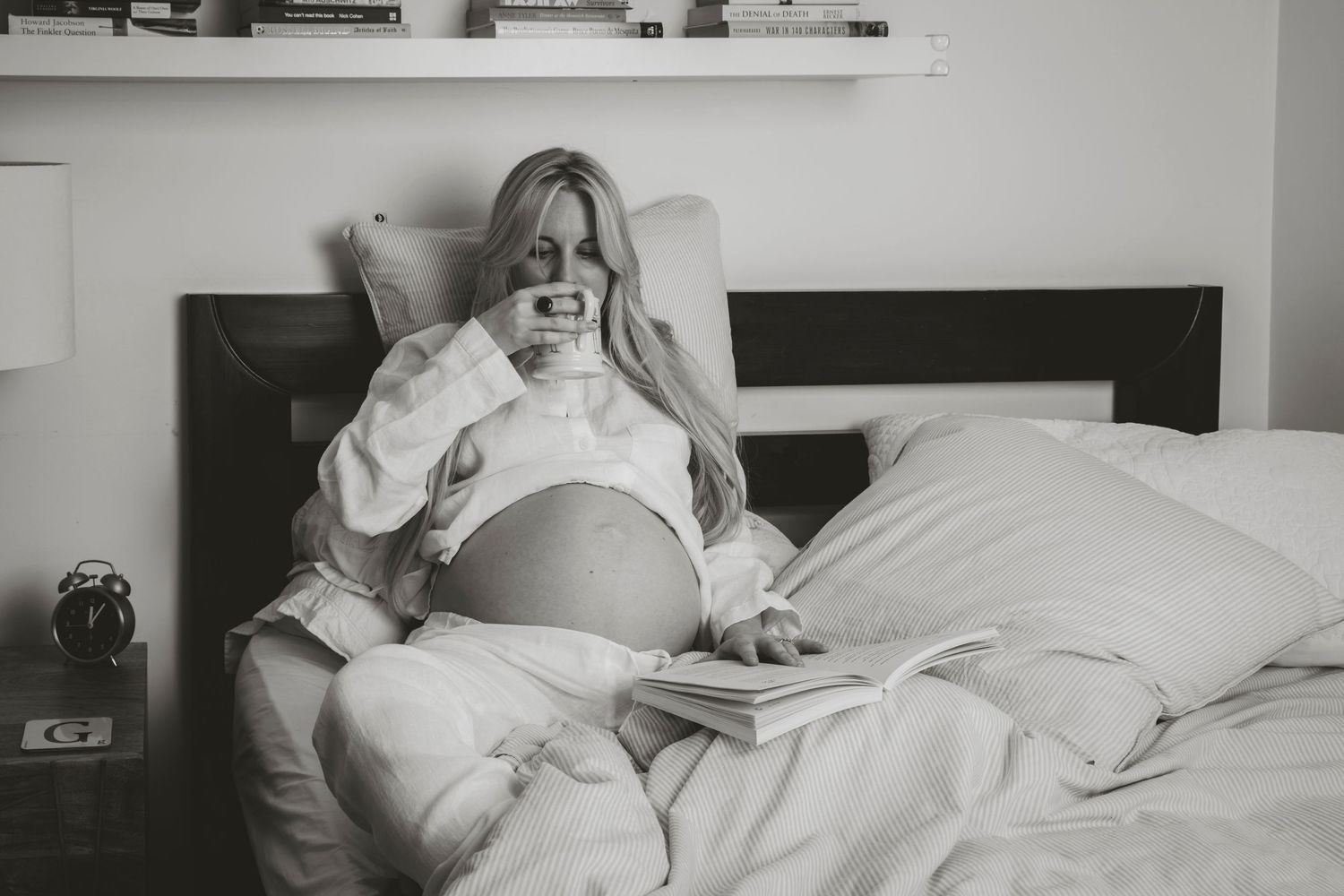 A relaxed maternity photo of an expectant mother resting in bed in black and white.