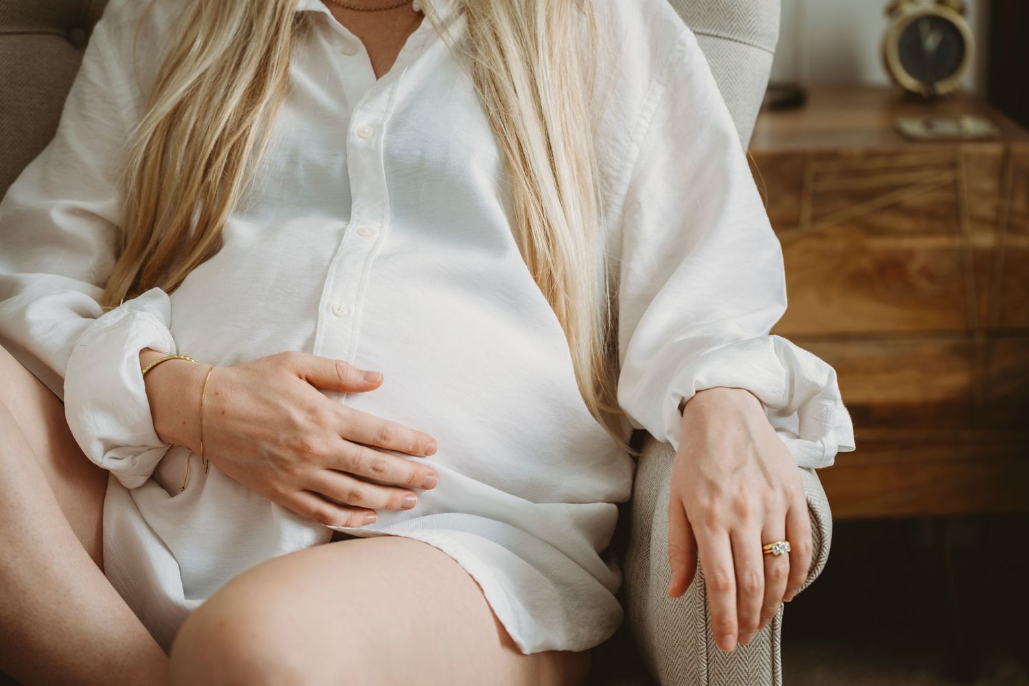 Detail shot of hands resting on pregnant belly in white button-down shirt.