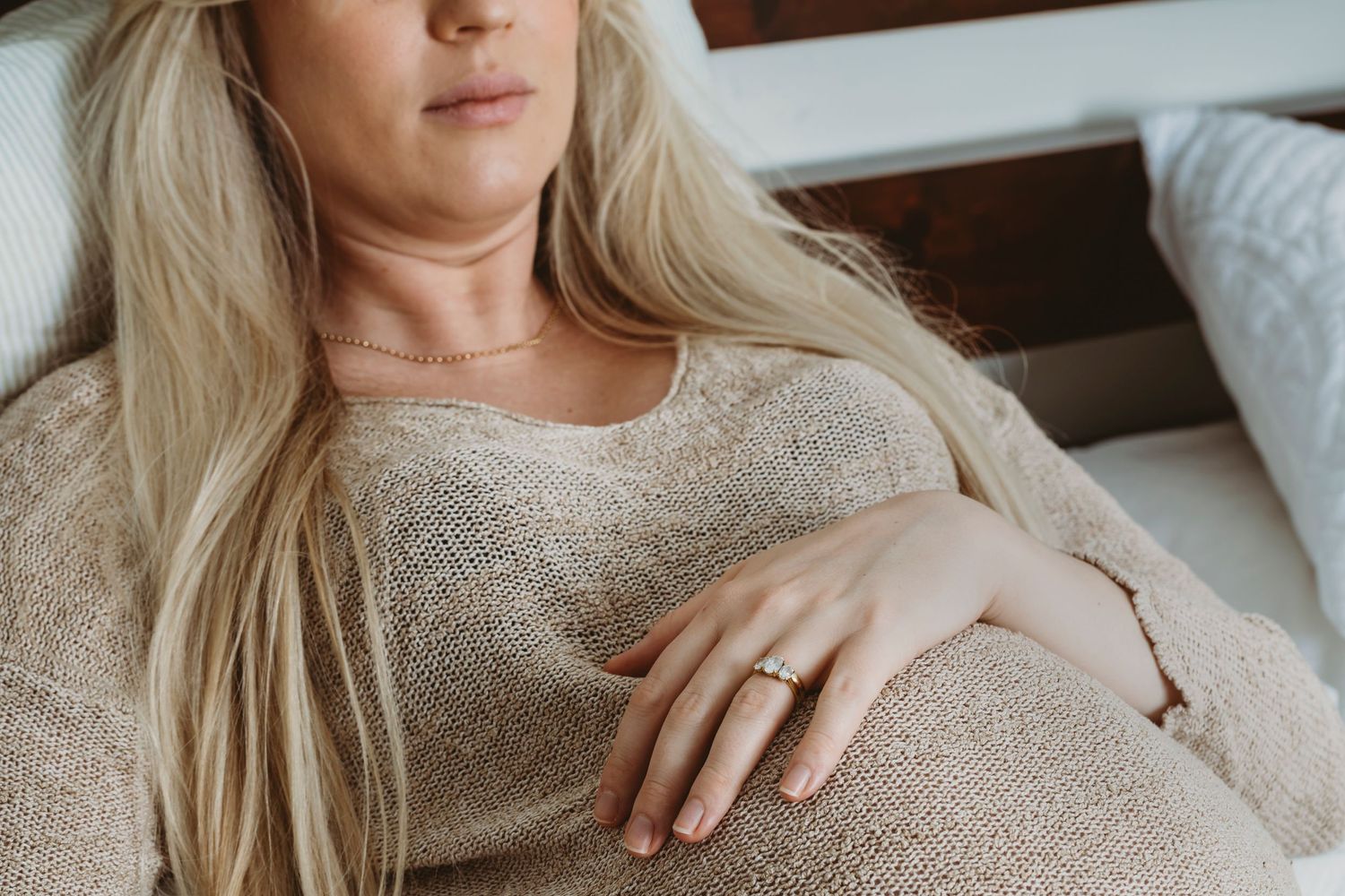 Close up of pregnant belly with hand wearing engagement ring resting on sweater.