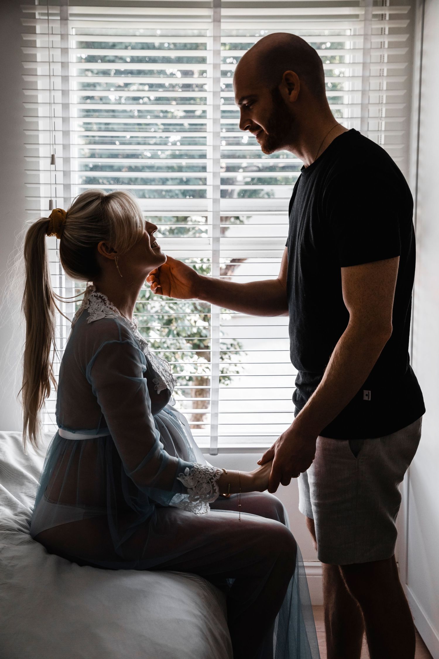 Silhouette of couple sharing tender moment by window during maternity session.