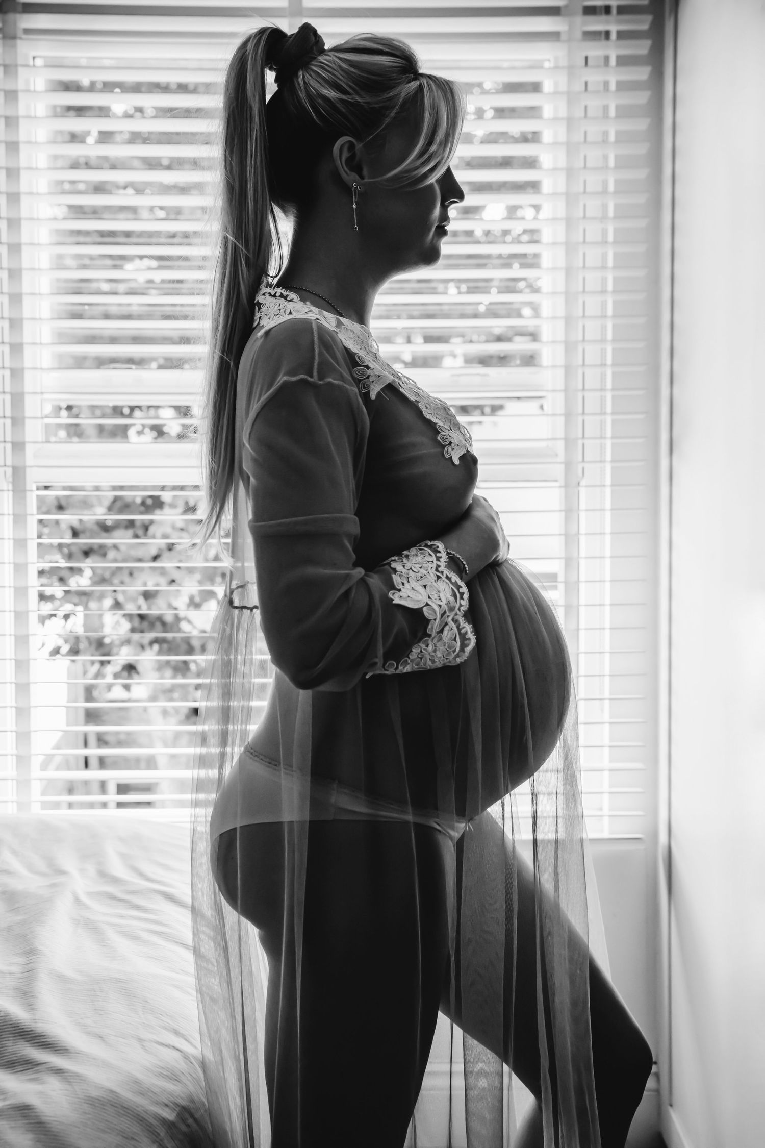 Silhouette of an expectant mother in lingerie standing by window with dramatic lighting.