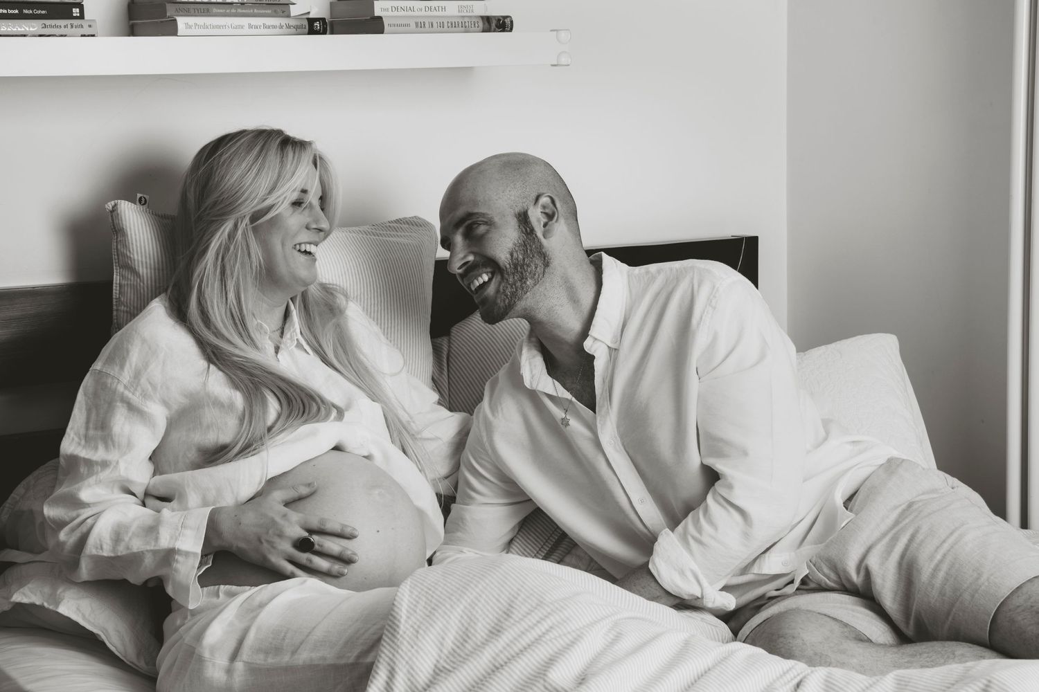 An intimate black and white photo of expecting parents sharing a tender moment on their bed, in Stoke Newington, London.
