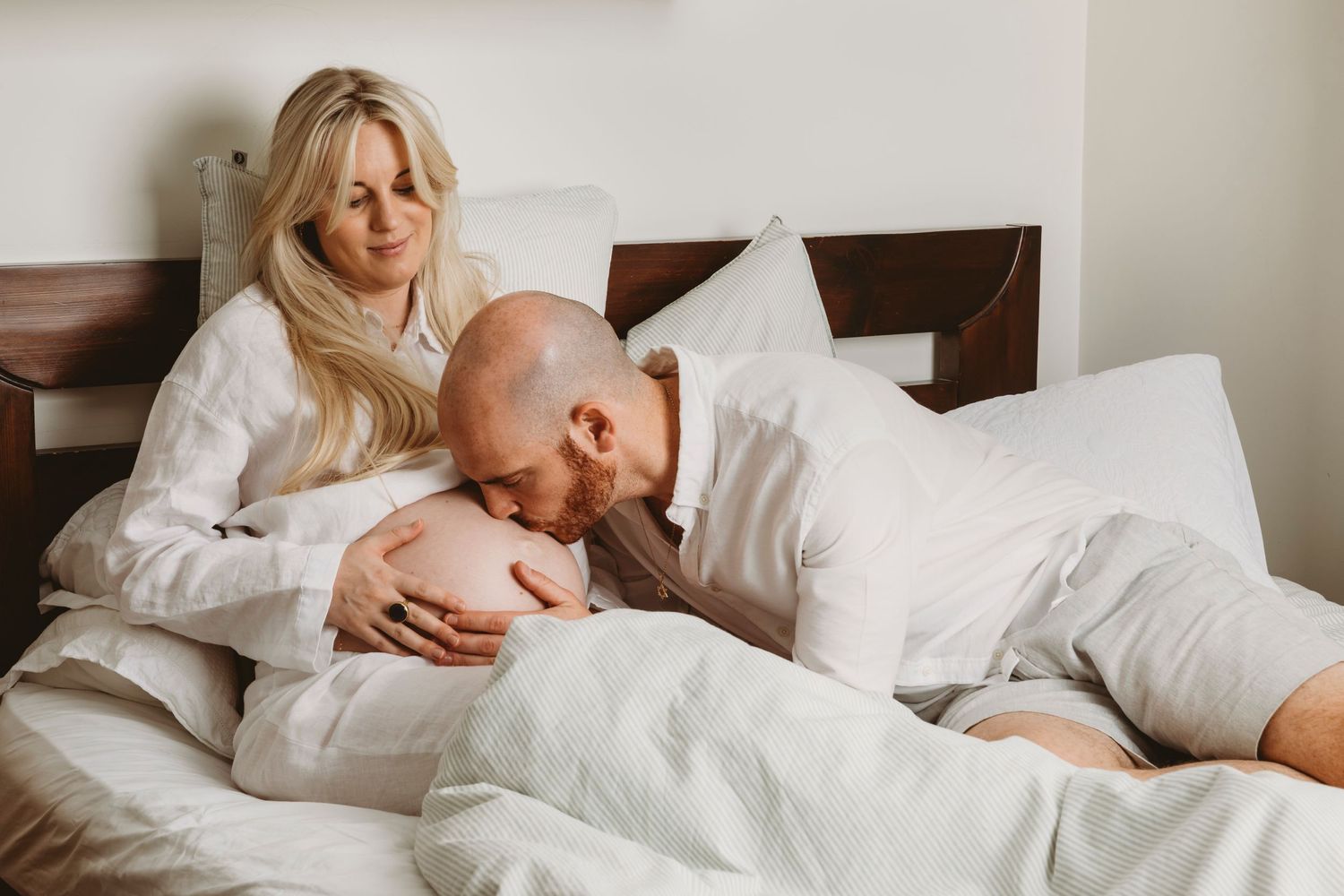 Intimate maternity moment between couple relaxing in white bed.
