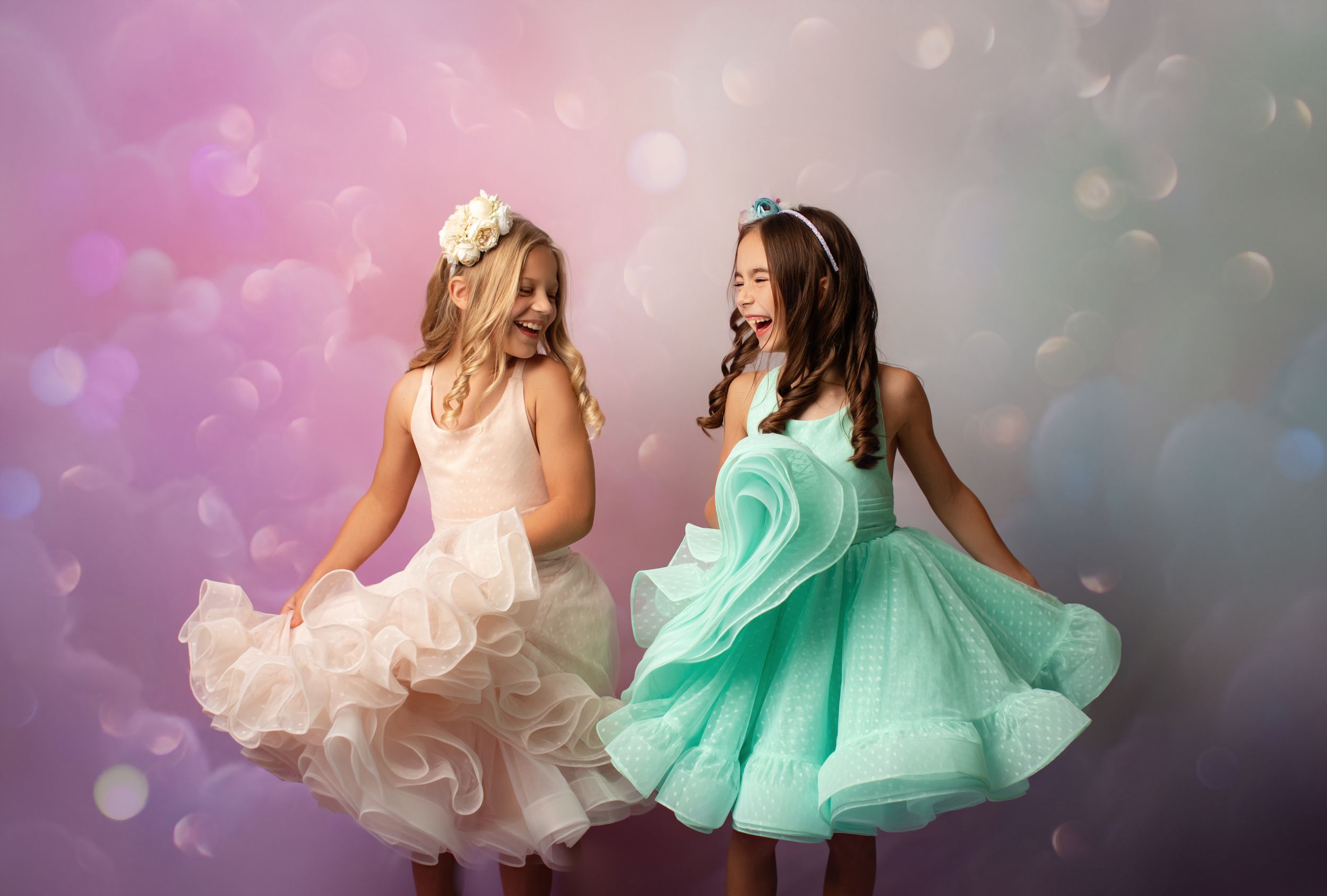 Two dancers twirling in pastel tulle dresses against dreamy bokeh backdrop.