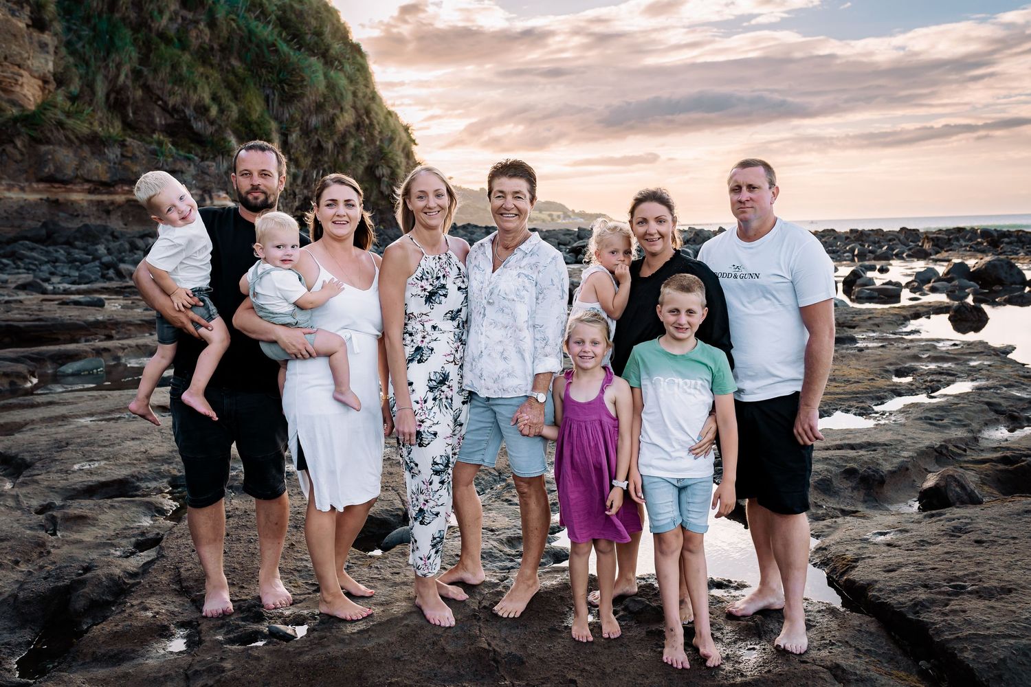 Extended family portrait at sunset on a rocky beach coastline.
