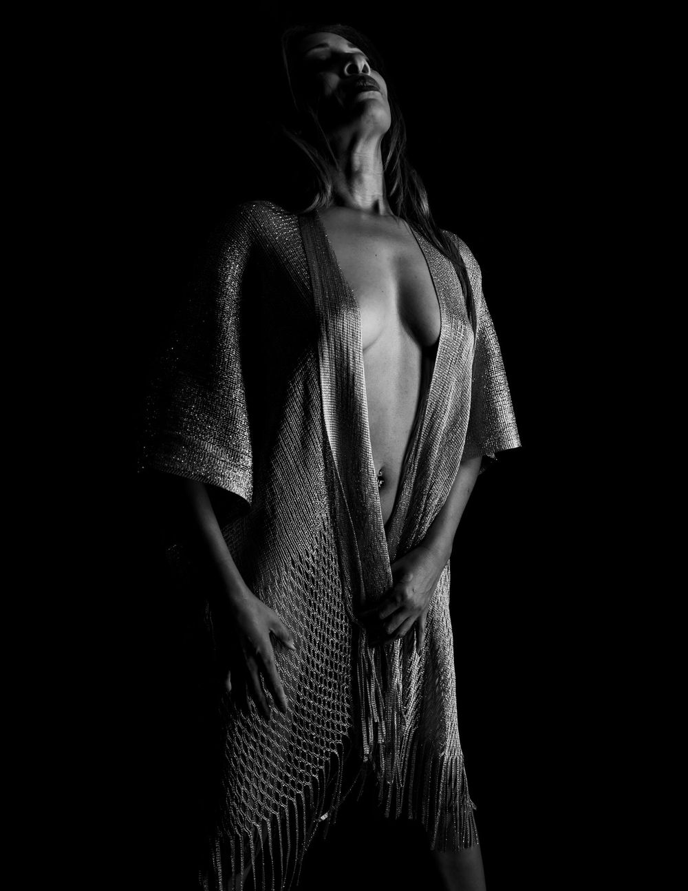 A black and white artistic portrait showing a person in dramatic lighting wearing a loose knit shawl.