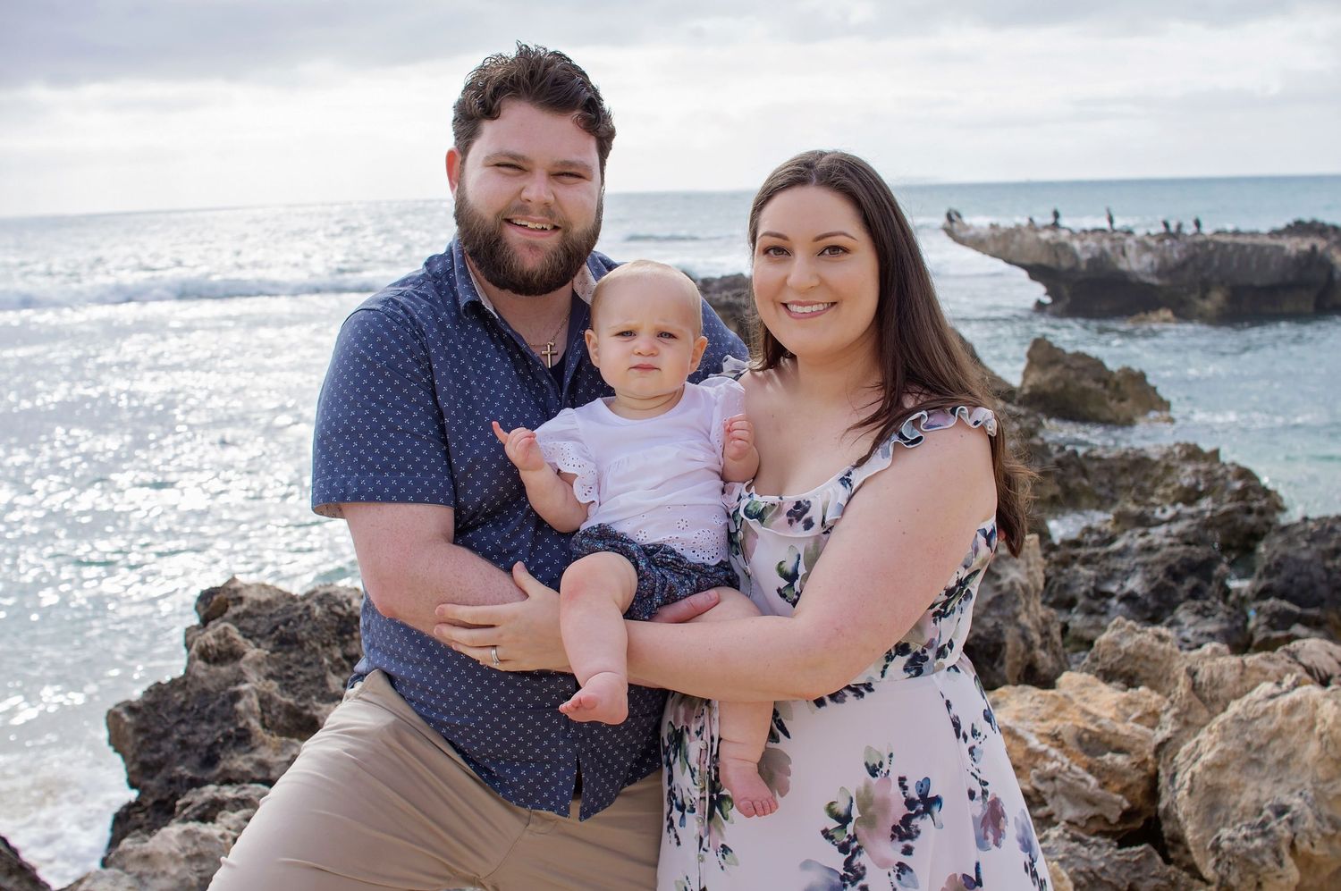 mother and father holding baby smiling at camera on beach