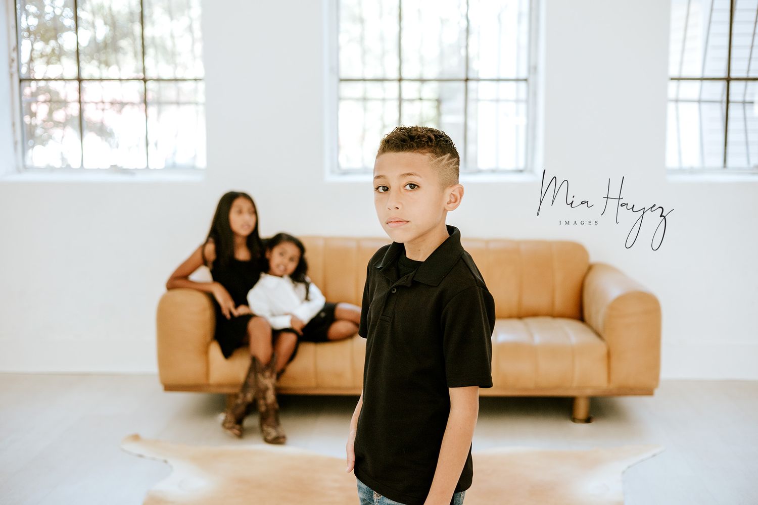 Minimalist indoor photo session featuring a couple on a tan couch in a bright white studio space.