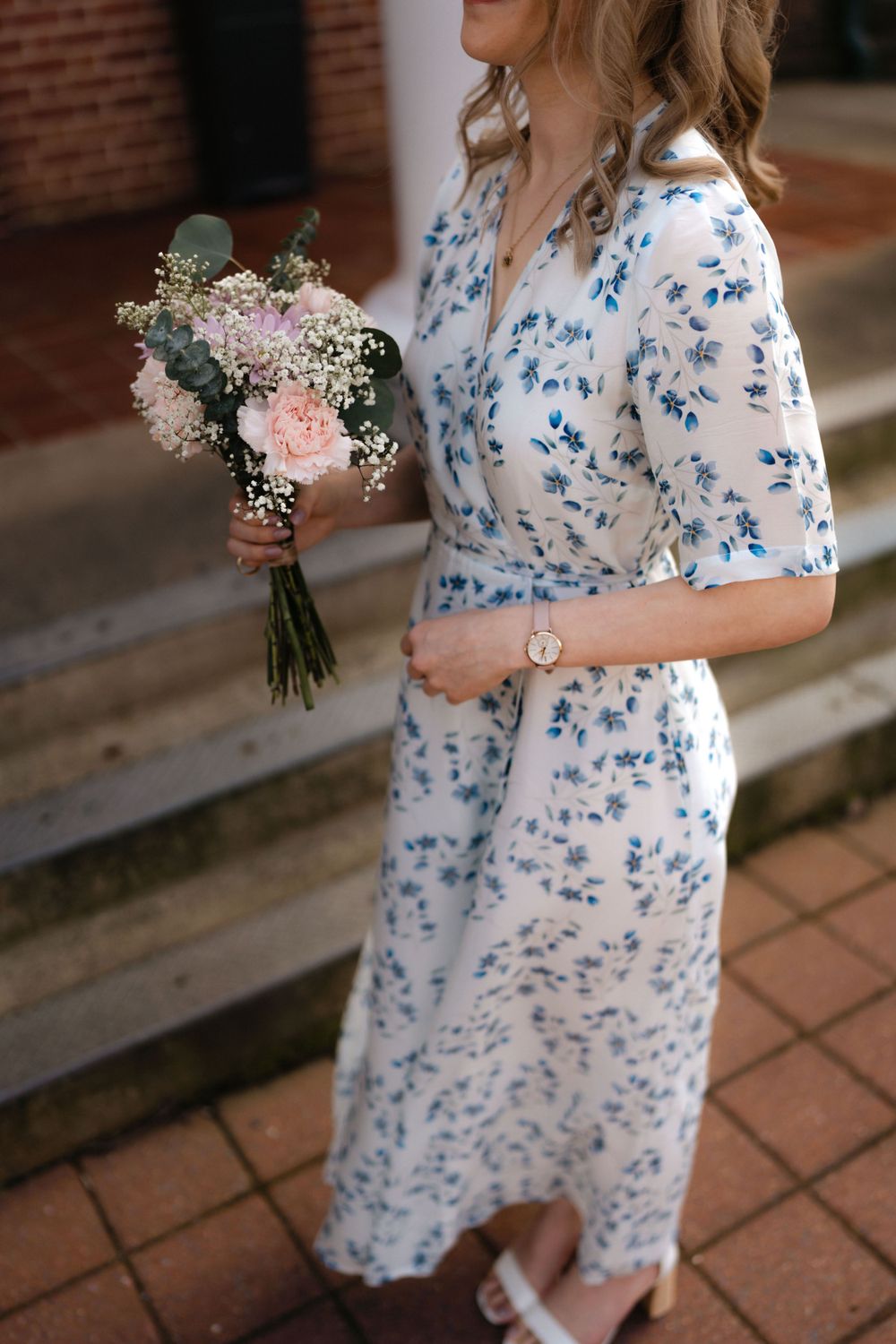 A delicate floral bouquet with pink roses and baby's breath held against a blue and white patterned dress.